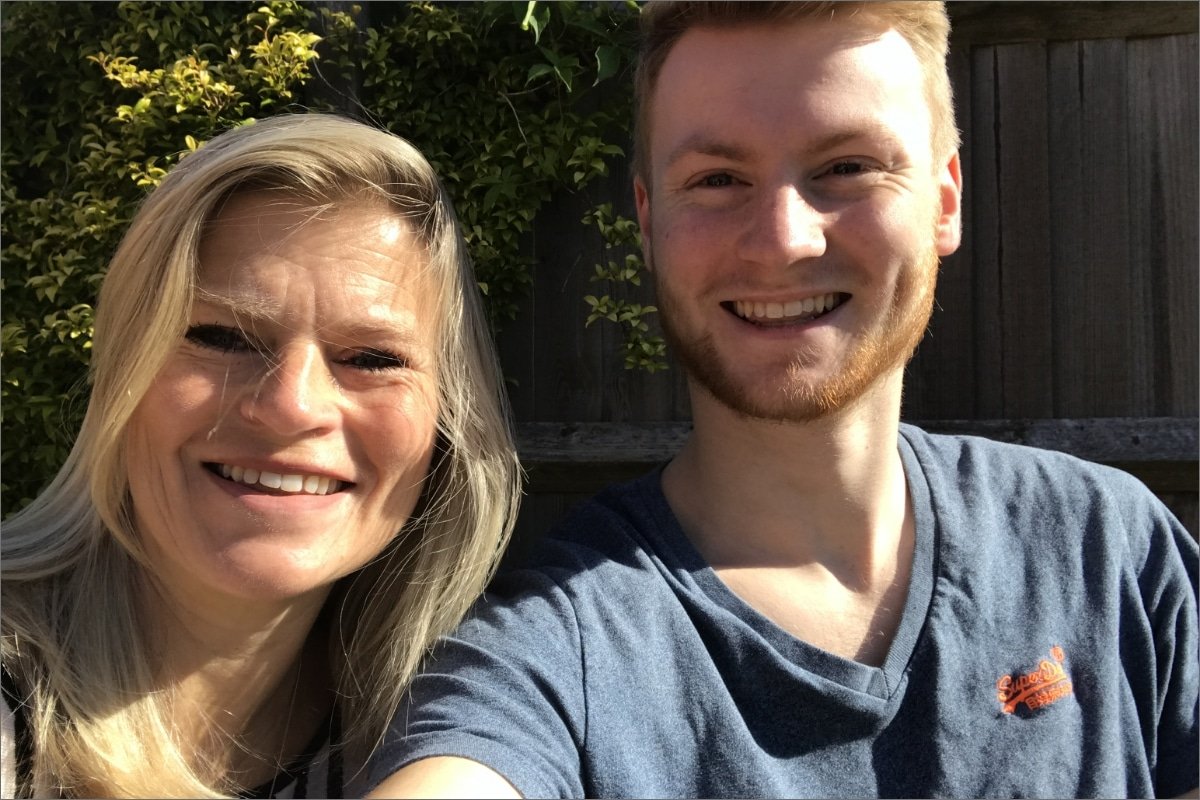 A woman and a young man smiling for a selfie outdoors.